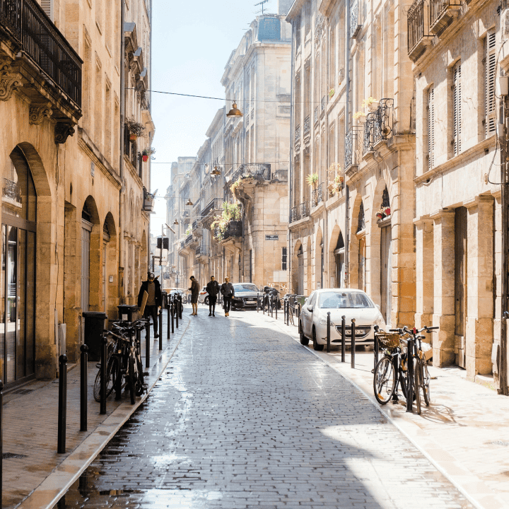 Rue pavée ensoleillée du centre-ville de Bordeaux avec façades en pierre typiques, vélos et piétons – ambiance urbaine chic près de la boutique Bob Corner, concept store décoration